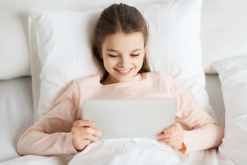 Image showing happy girl lying in bed with tablet pc at home