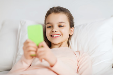 Image showing happy girl lying in bed with smartphone at home