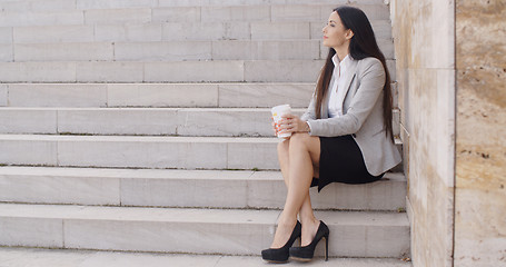 Image showing Grinning woman on stairs drinking coffee