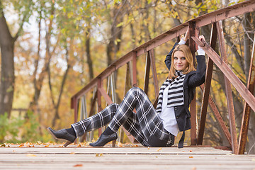 Image showing Happy girl sitting on a bridge in the forest and looking at the frame