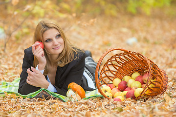 Image showing Young beautiful girl lies on the on the foliage in the autumn forest and dreaming holding an apple and looking to the right