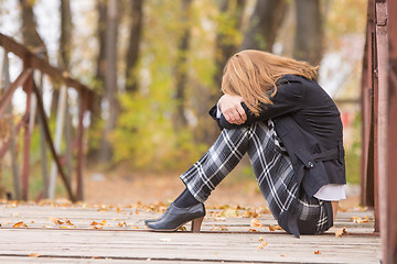 Image showing Sad girl sitting on a bridge with her head resting on his knees