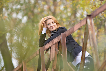 Image showing Young beautiful girl standing on the bridge, leaning on the railing and looking pensively into the distance