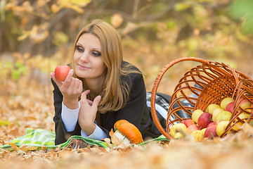 Image showing Young beautiful girl lies on the on the foliage in autumn forest and looking at an apple in her hand