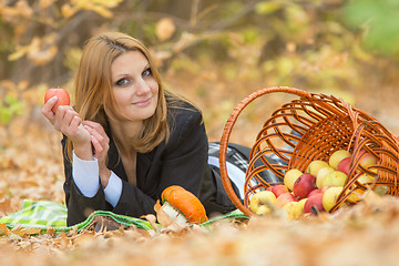 Image showing Young beautiful girl lies on the on the foliage in the autumn forest and holding an apple in her hand