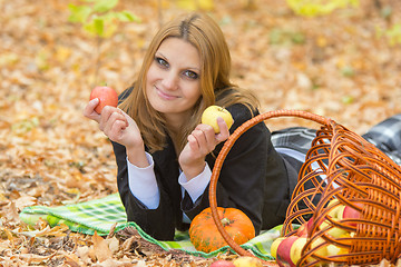 Image showing Young girl lying on a rug in the autumn forest and holding two apples in the hands of