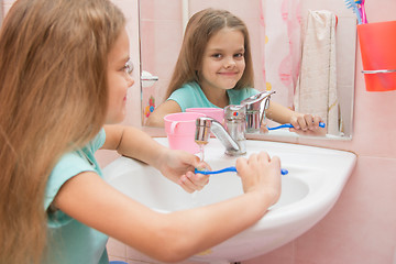 Image showing The girl washes a toothbrush under the tap