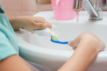 Image showing The child squeezes the toothpaste from a tube on toothbrush