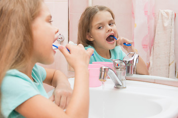 Image showing Six year old girl cleans the lower lateral teeth look in the mirror in the bathroom