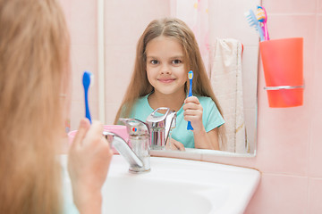 Image showing Six year old girl opening her mouth treats teeth in reflection in a mirror, while in the bathroom