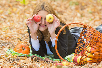Image showing Young beautiful girl lying on the leaves in the autumn forest in the fun and put the apples to the eyes