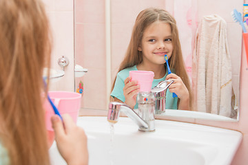 Image showing Girl standing with a toothbrush and a glass in the bathroom