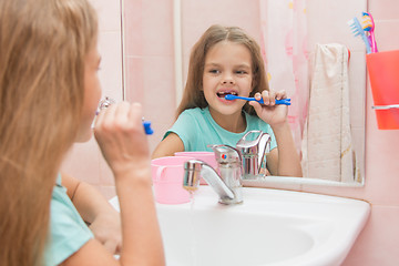 Image showing Six year old girl cleans the lower front teeth look in the mirror in the bathroom