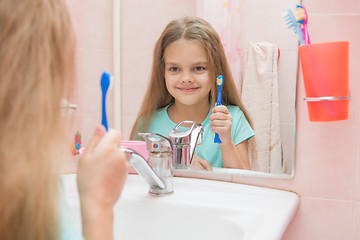 Image showing  Six year old girl holding a toothbrush and looks at himself in the mirror, while in the bathroom