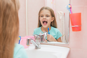 Image showing Six year old girl opening her mouth treats teeth in reflection in a mirror, while in the bathroom