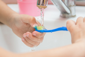 Image showing Child washes toothbrush under running water, close-up