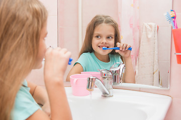 Image showing Six year old girl brushing the front teeth look in the mirror in the bathroom