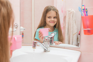 Image showing Happy girl holding a cup and looks in the mirror in the bathroom