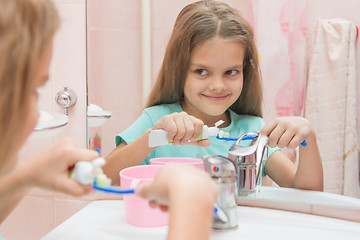 Image showing Happy little girl squeezes the toothpaste from a tube on toothbrush