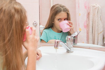 Image showing Girl dials the water in the mouth from the cup by rinsing the mouth after brushing