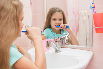 Image showing Six year old girl cleans teeth side looking in the mirror in the bathroom
