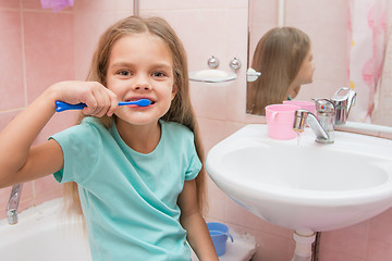 Image showing Six year old girl brushing her teeth and turned away from the sink looks in the picture