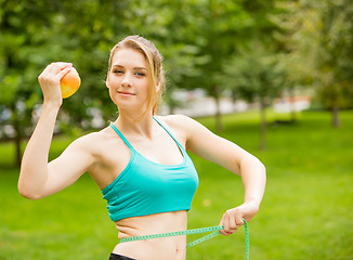 Image showing Sporty young woman with apple and measuring tape. Outdoors. 