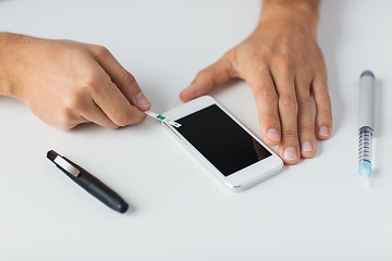 Image showing close up of man with smartphone making blood test