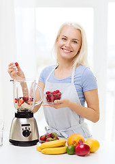 Image showing smiling woman with blender preparing shake at home