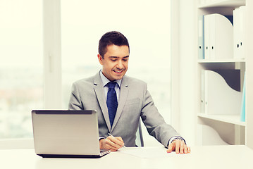 Image showing smiling businessman with laptop and papers