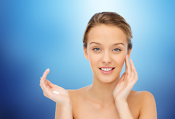 Image showing happy young woman applying cream to her face