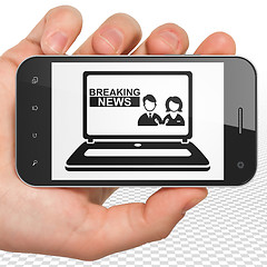 Image showing News concept: Hand Holding Smartphone with Breaking News On Laptop on display