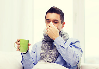Image showing ill man with flu drinking tea and blowing nose