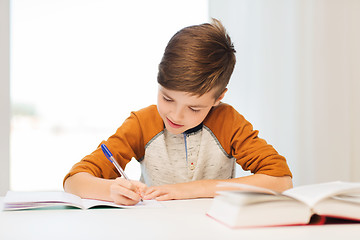 Image showing smiling student boy writing to notebook at home