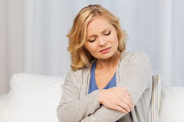 Image showing unhappy woman suffering from pain in hand at home