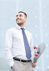 Image showing young smiling businessman with skateboard outdoors