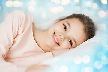 Image showing happy smiling girl lying awake in bed over lights