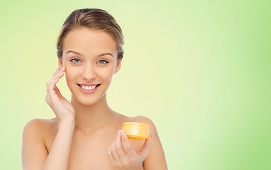 Image showing happy young woman applying cream to her face