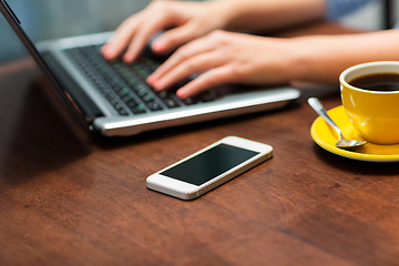 Image showing close up of smartphone and hands typing on laptop