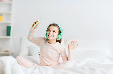 Image showing girl sitting on bed with smartphone and headphones