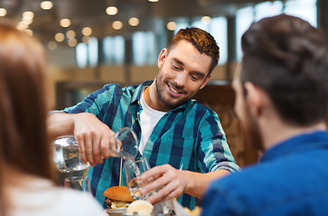 Image showing happy man with friends pouring water at restaurant