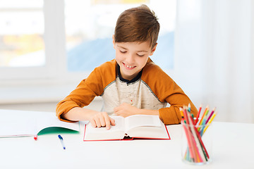 Image showing smiling, student boy reading book at home