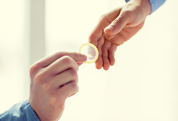 Image showing close up of male gay couple hands giving condom