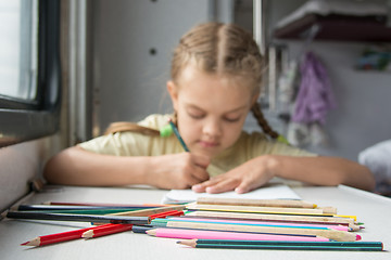 Image showing  Pencils in the foreground, in the background a six year old girl drawing pencils in a second-class train carriage