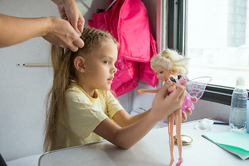 Image showing  A girl playing with dolls until my mother weave braid of hair
