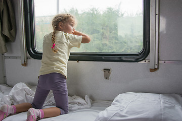 Image showing Four-year girl on the side of the shelf of the train looking out the window