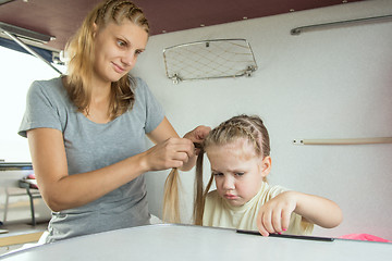 Image showing The girl is sick mother braids her pigtails, on a cot in a train