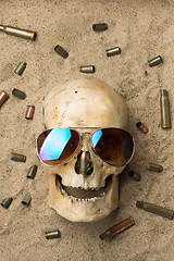 Image showing skull lying in the sand, scattered rifle and pistol cartridges. concept of war