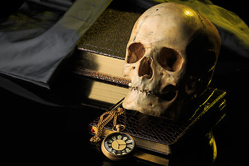 Image showing human skull on a book next to the clock. concept of black magic