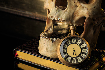 Image showing human skull on a book next to the clock. concept of black magic